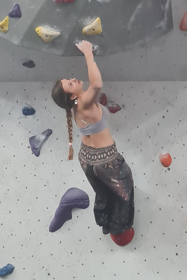 A women climbing a overhanging indoor boulder problem looking up